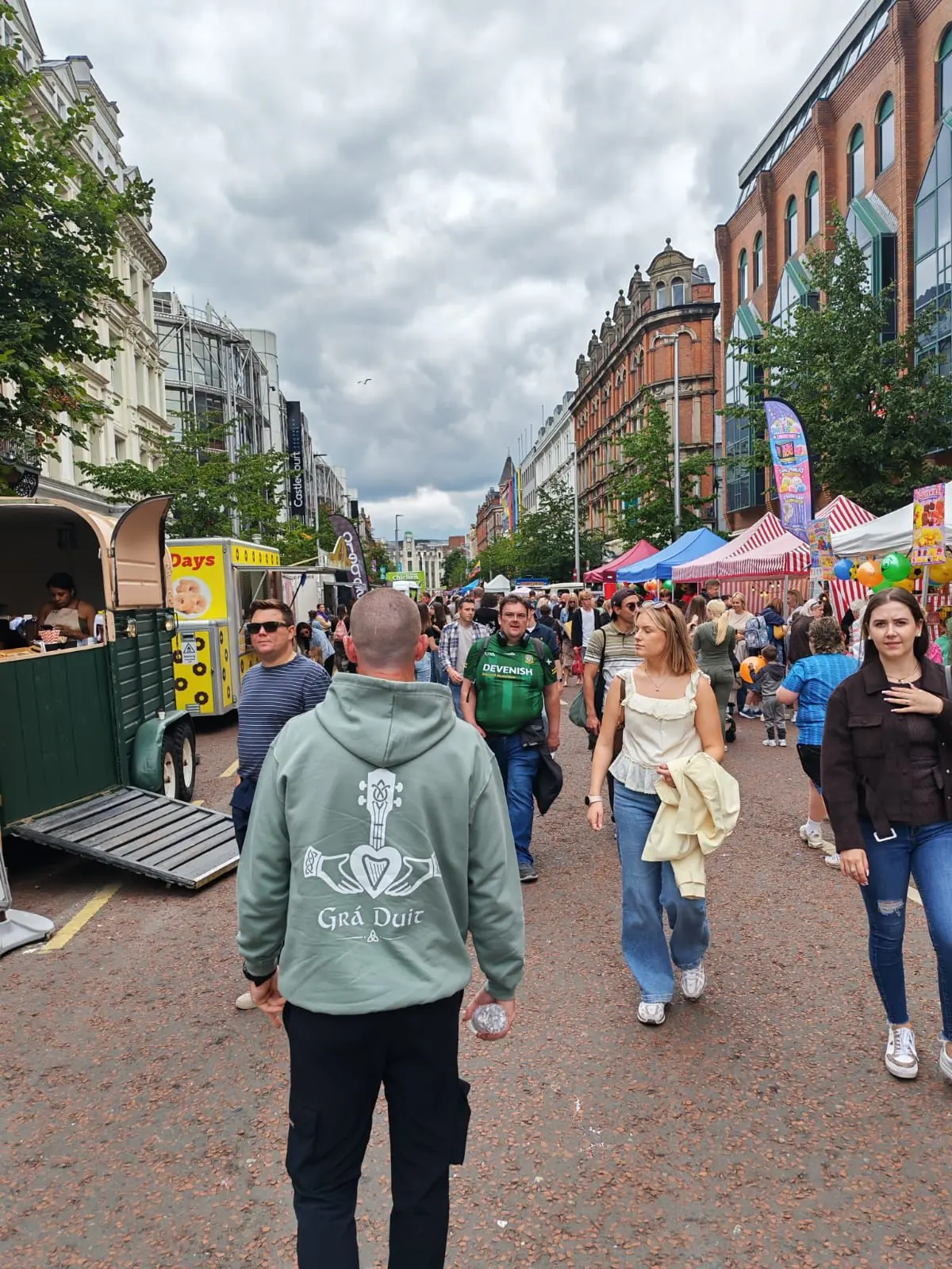 Dusty Green Grá Duit hoodie worn at a community market